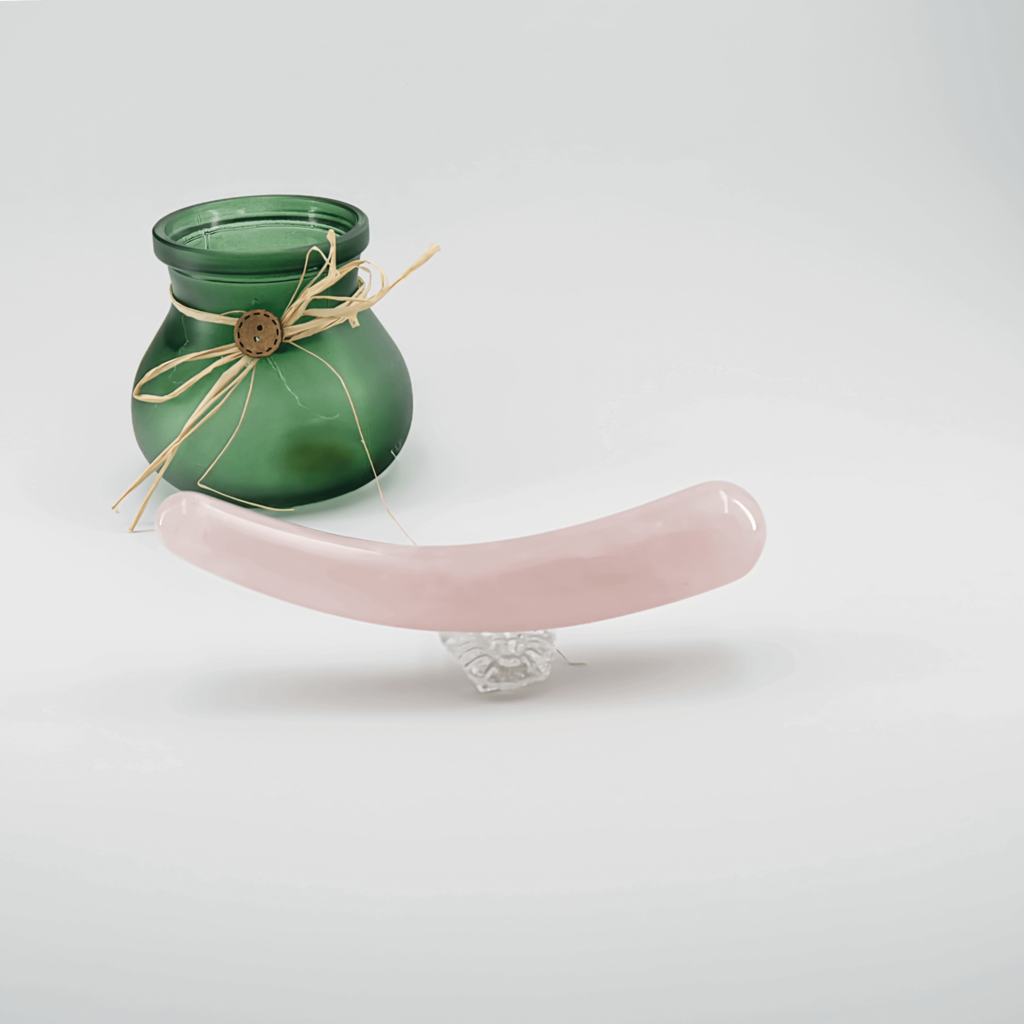 A rose quartz crystal wand beside a green candle, showcasing wellness and intimate self-care tools.