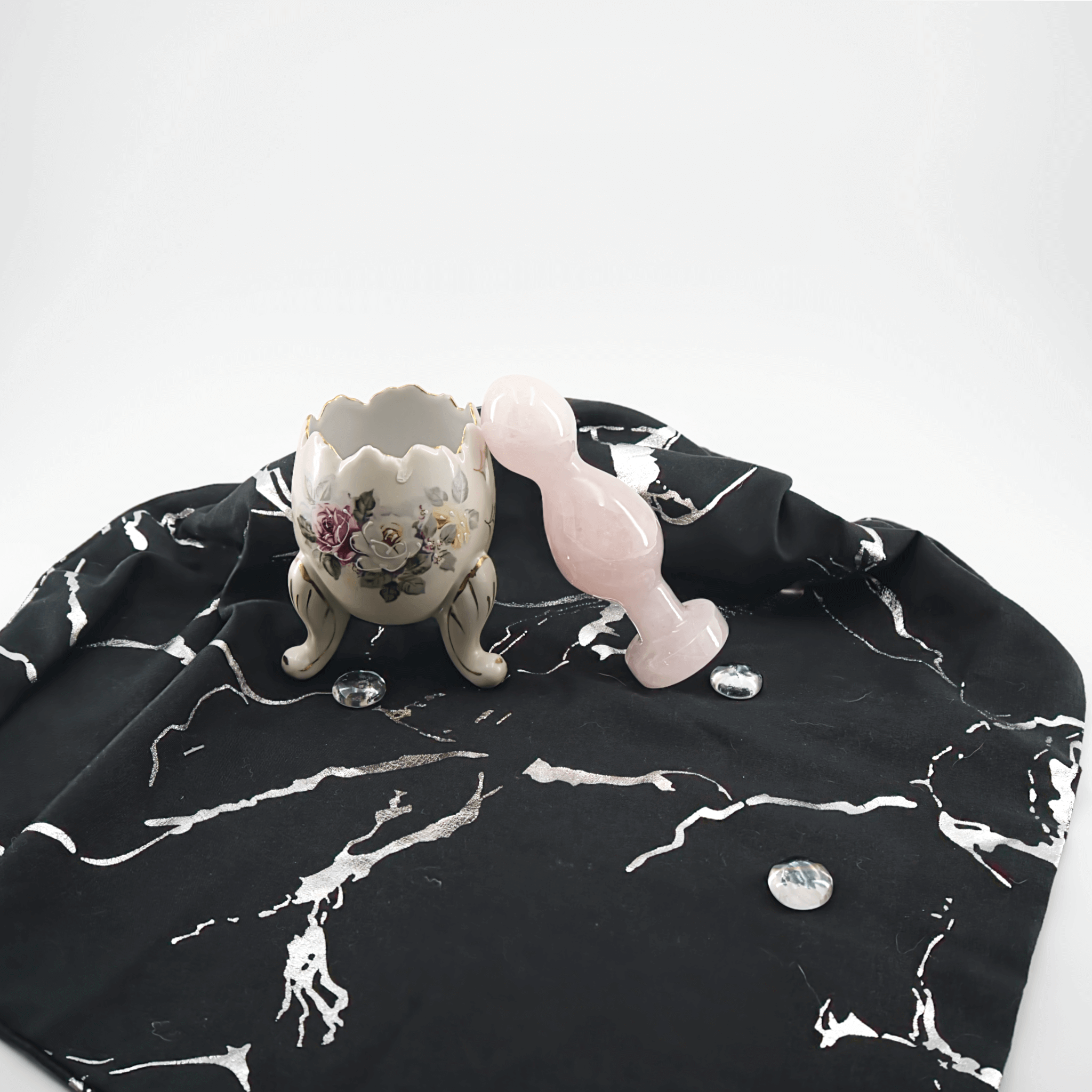 A pink crystal wand beside a decorative ceramic holder on a stylish black and white fabric background.