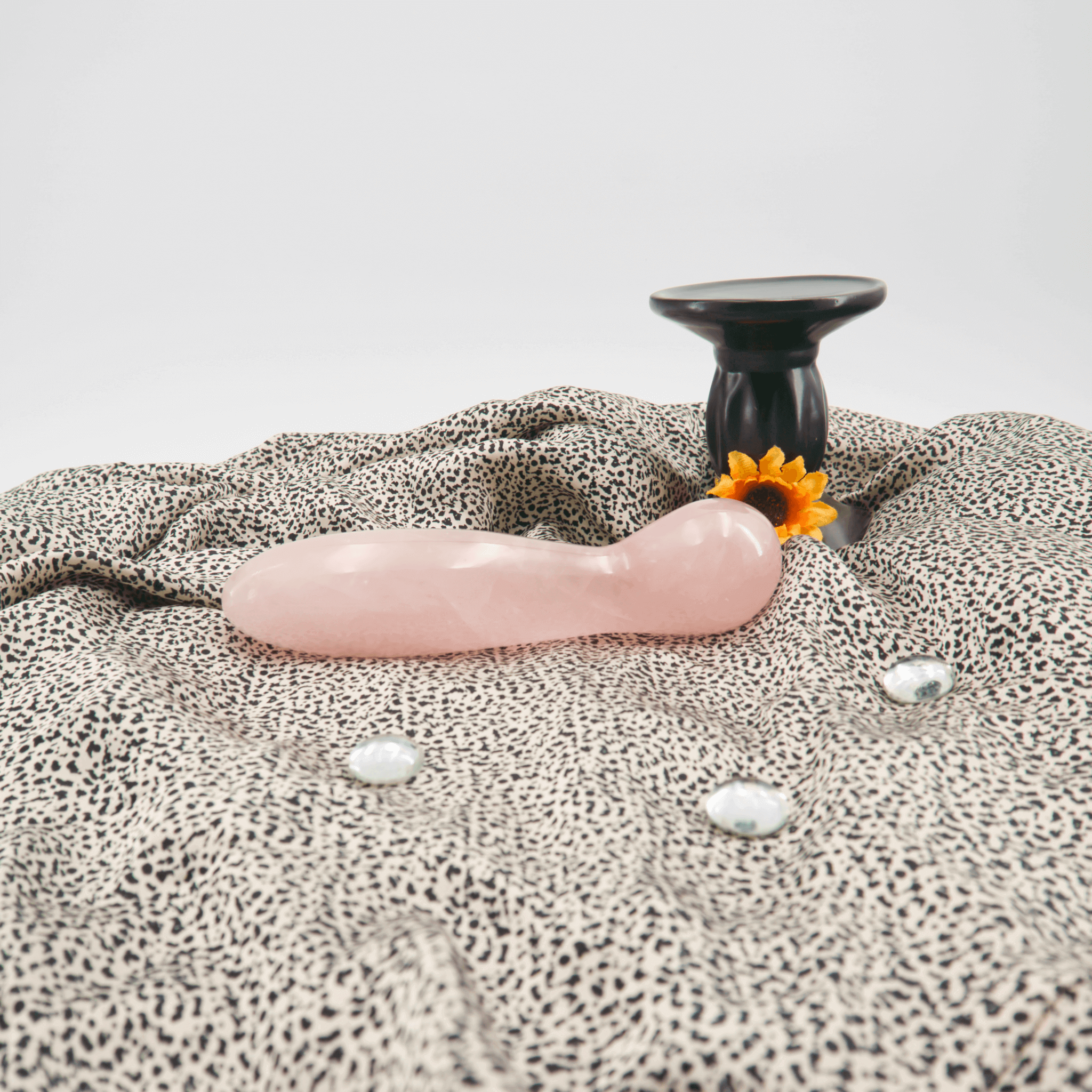 Hand-carved rose quartz crystal wand on patterned fabric with decorative stones and a black sculpture.