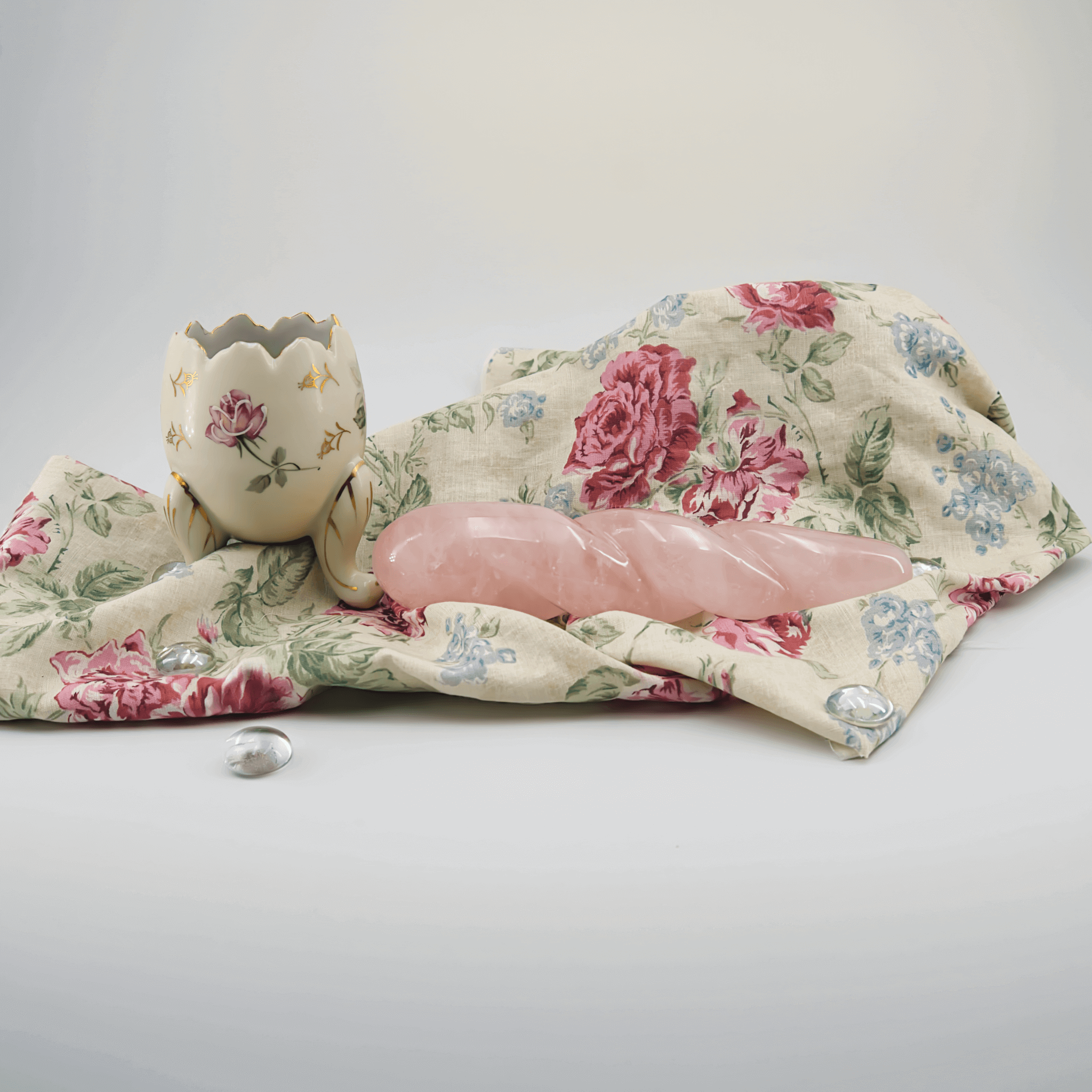 A pink crystal wand beside a decorative egg holder on a floral cloth, symbolizing crystal healing.
