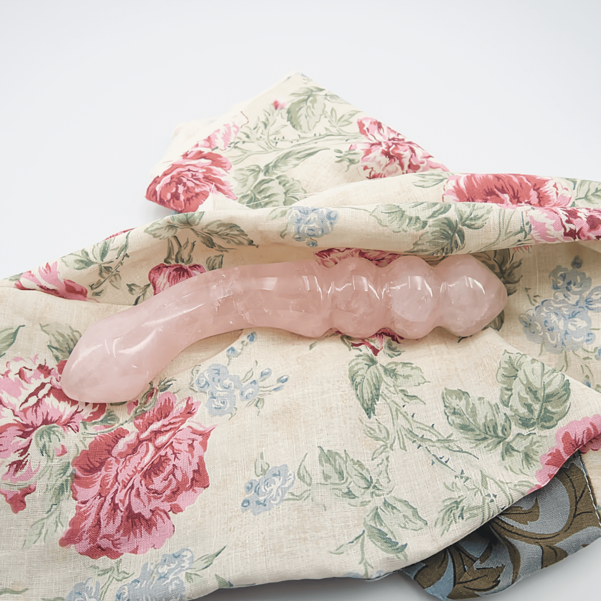 Rose quartz crystal wand on floral fabric, symbolizing self-care and wellness.