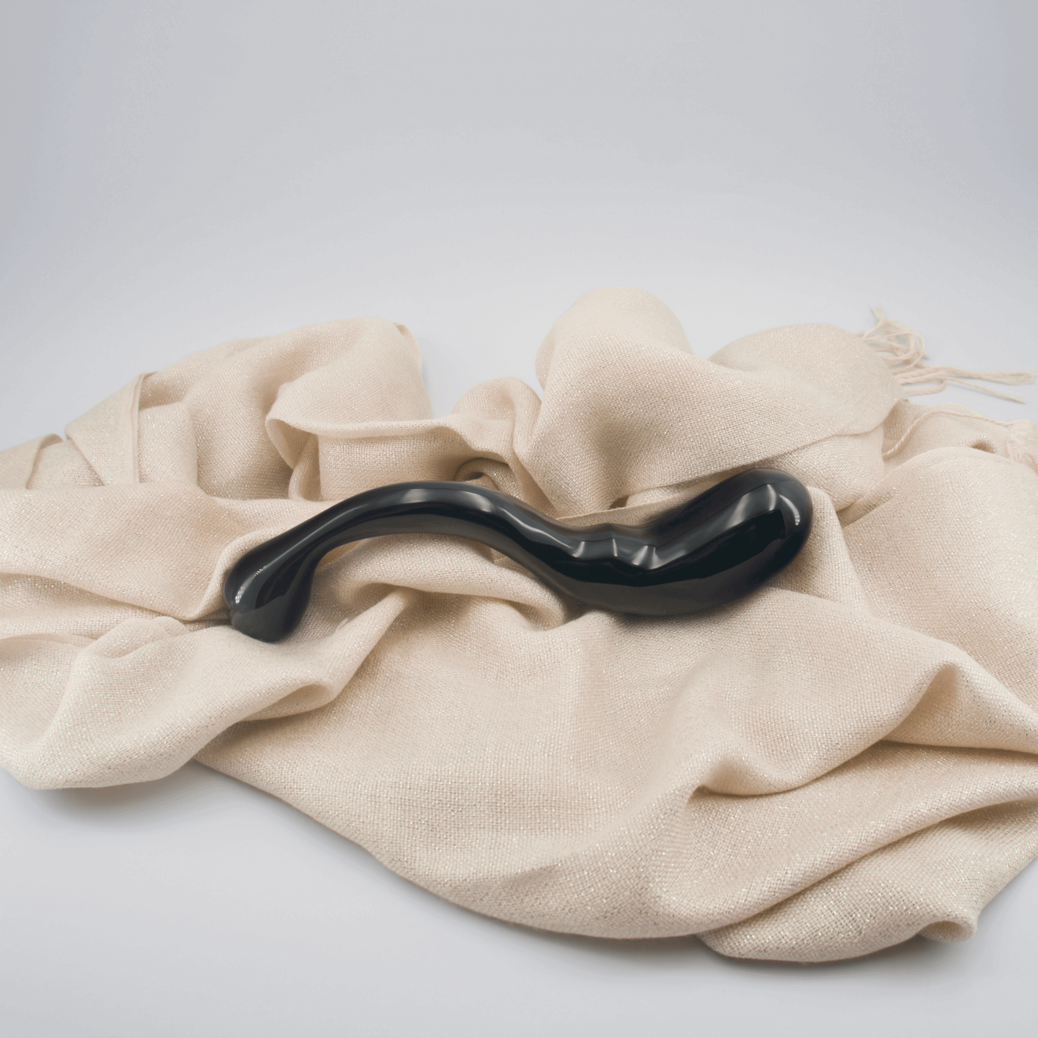 Elegant black crystal wand resting on soft beige fabric, showcasing its smooth curves and unique design.