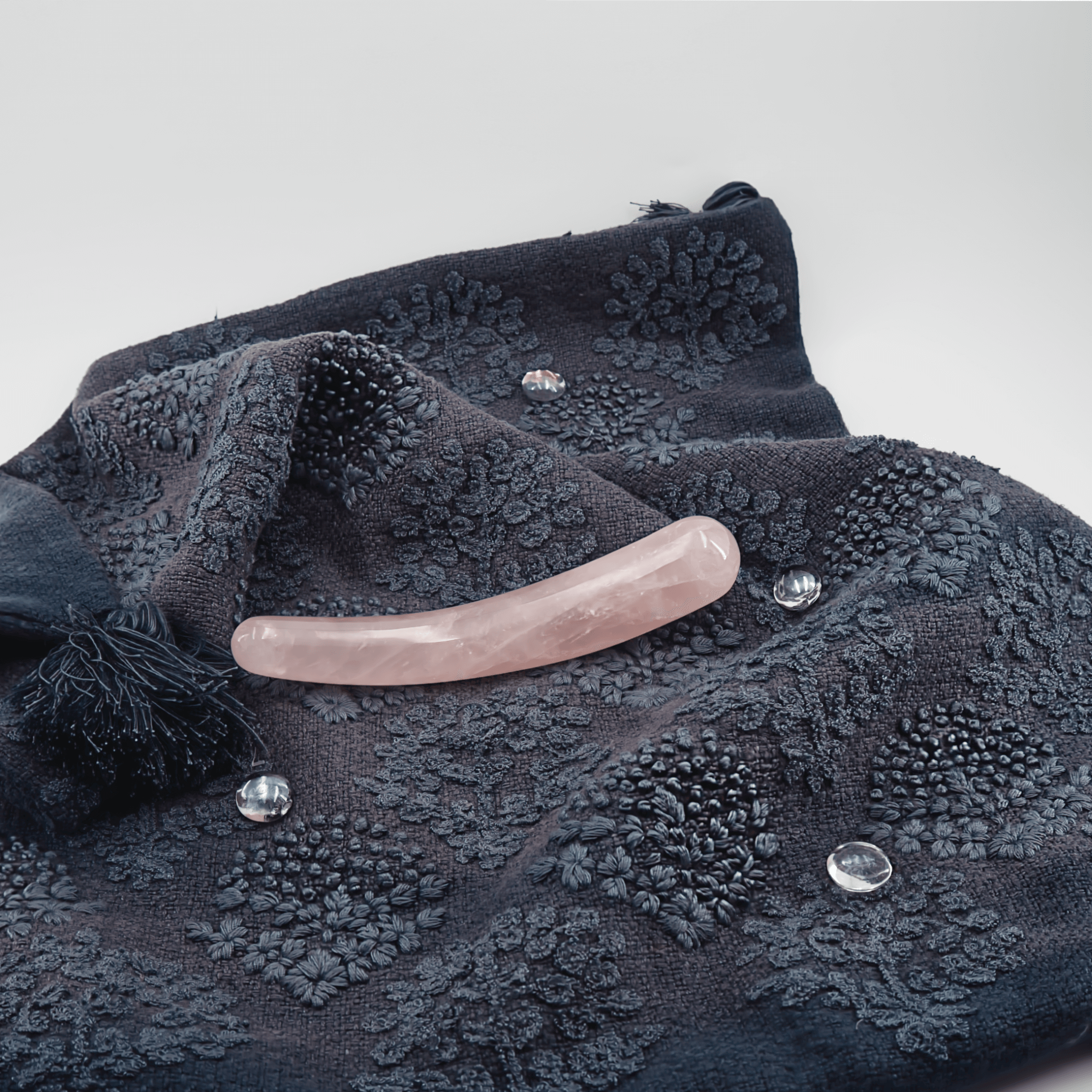 Soft pink crystal wand on textured dark fabric with sparkling gemstones, ideal for meditation and energy work.